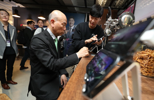 이효성 방송통신위원회 위원장이 17일 서울 강남역 인근에 위치한 5G 체험관(LGU+ 일상로5G길)에서 프로야구 애플리케이션(앱)을 시연하고 있다.  LG유플러스 제공